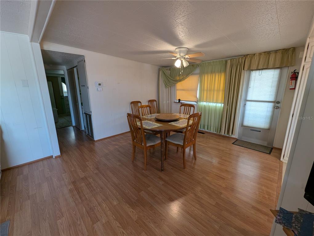A dining area features a round wooden table with four chairs, wood-look flooring, and curtains — 107 48TH AVENUE DRIVE W, BRADENTON, FL