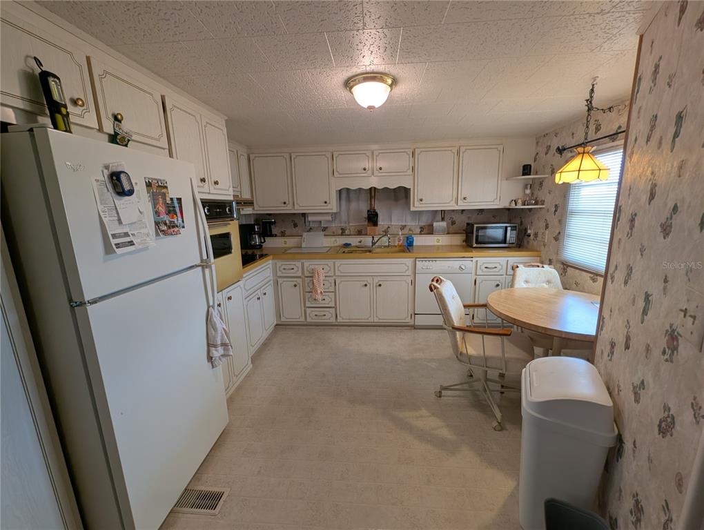 A kitchen with white cabinets, yellow countertops, a dining table, and floral wallpaper — 107 48TH AVENUE DRIVE W, BRADENTON, FL