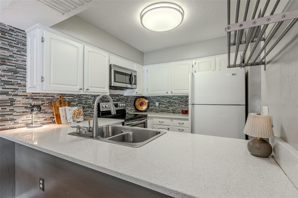 A kitchen features white cabinets, a stainless steel microwave, a white refrigerator, and quartz countertops — 4460 SW 20TH LANE, GAINESVILLE, FL
