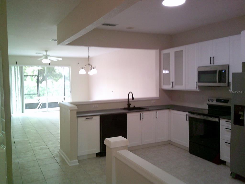 A kitchen with white cabinets, black appliances, and a pass-through window overlooking the living area — 6292 TWAIN STREET UNIT 107, ORLANDO, FL