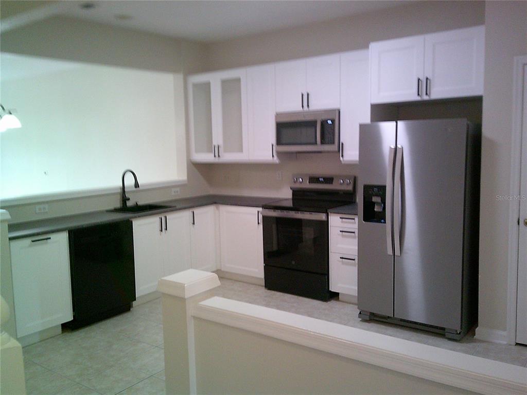 A kitchen features white cabinets, dark countertops, stainless steel appliances, and a black sink — 6292 TWAIN STREET UNIT 107, ORLANDO, FL