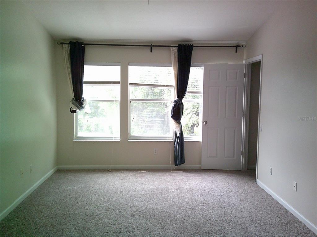 An empty bedroom features beige carpet, light-colored walls, two windows, and a white door — 6292 TWAIN STREET UNIT 107, ORLANDO, FL