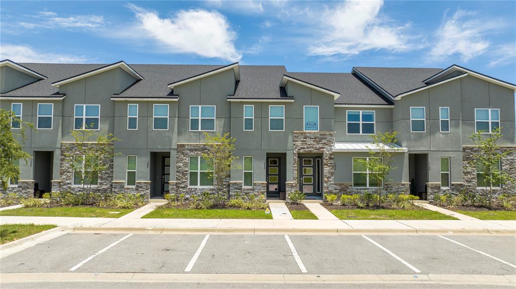 A row of modern two-story townhomes with gray siding, stone accents, and a parking lot — 1692 TROPICAL PALMS CIRCLE, KISSIMMEE, FL