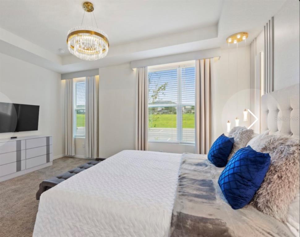 A bedroom features a crystal chandelier, a king bed with blue pillows, and large windows — 1692 TROPICAL PALMS CIRCLE, KISSIMMEE, FL