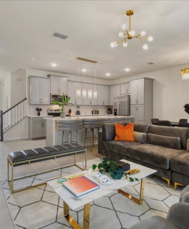 An open-concept kitchen and living area featuring grey cabinetry, a marble-topped island, and gold accents — 1692 TROPICAL PALMS CIRCLE, KISSIMMEE, FL