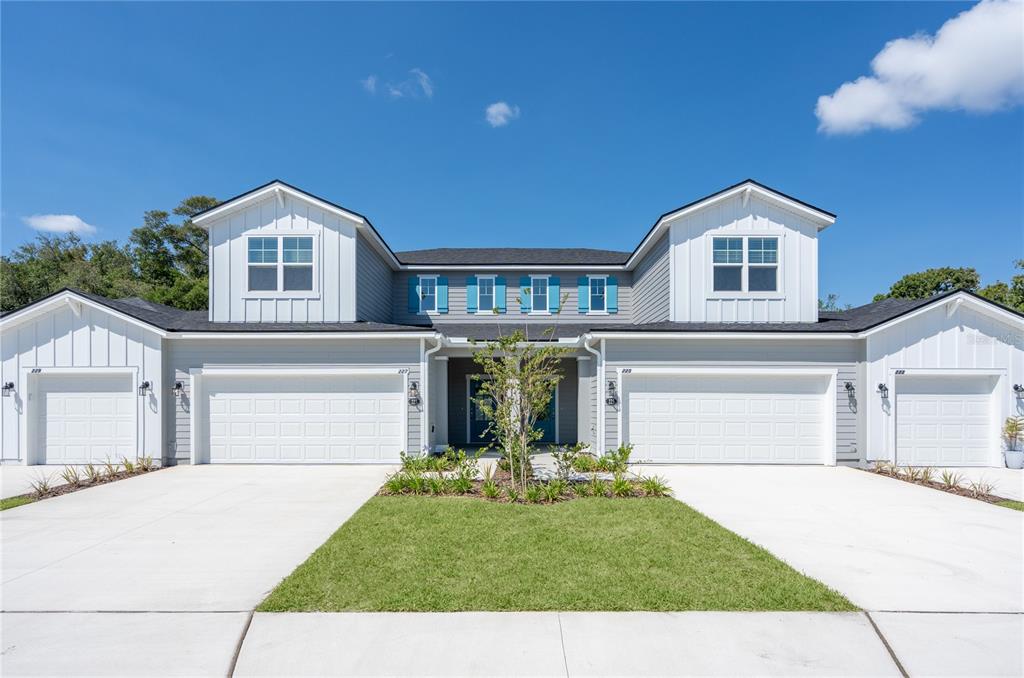 A two-story duplex with white siding, blue shutters, and four garage doors under a blue sky — 212 MISTY HARBOR TRACE, PALM COAST, FL