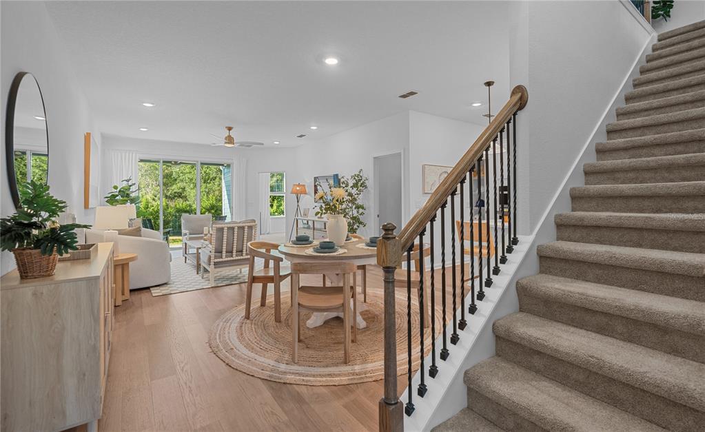 A bright open-concept living and dining area features wood flooring, a staircase, and patio doors — 212 MISTY HARBOR TRACE, PALM COAST, FL