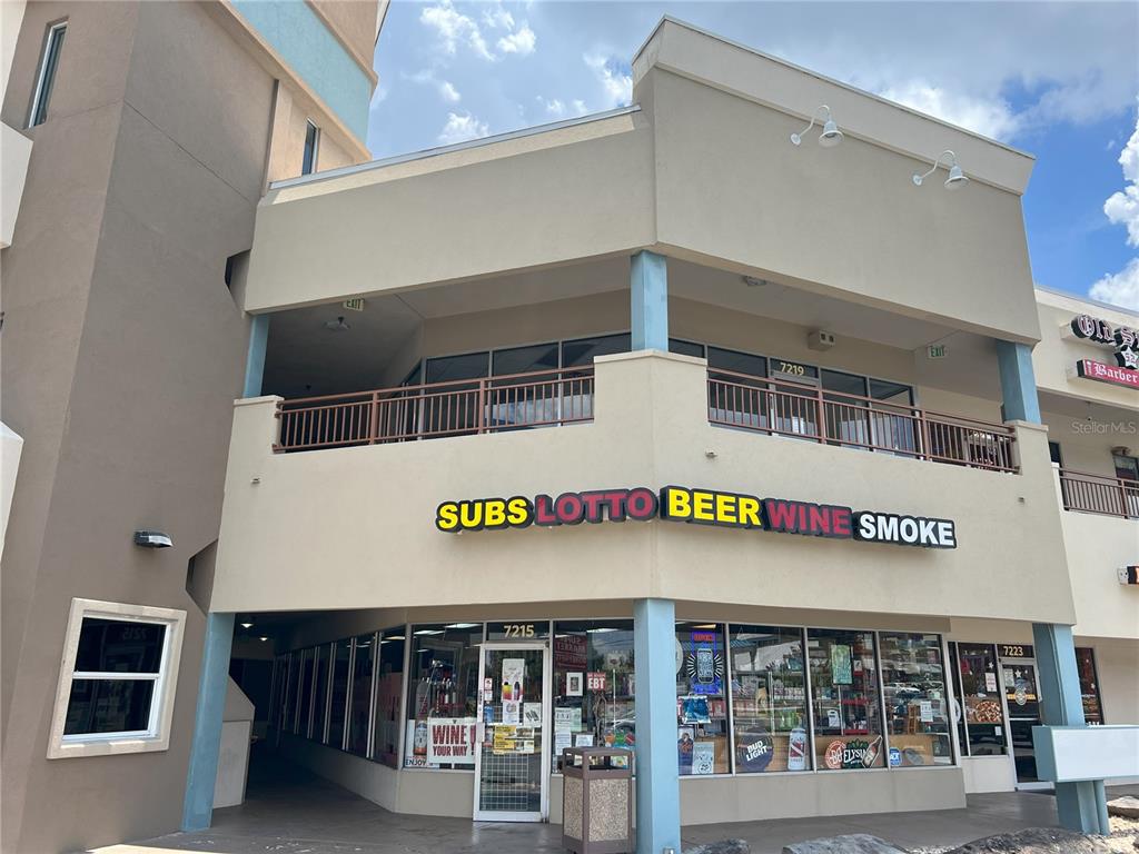 A commercial storefront features signage for subs, lotto, beer, wine, and smoke with upper-level balconies — 7219 INTERNATIONAL DRIVE, ORLANDO, FL