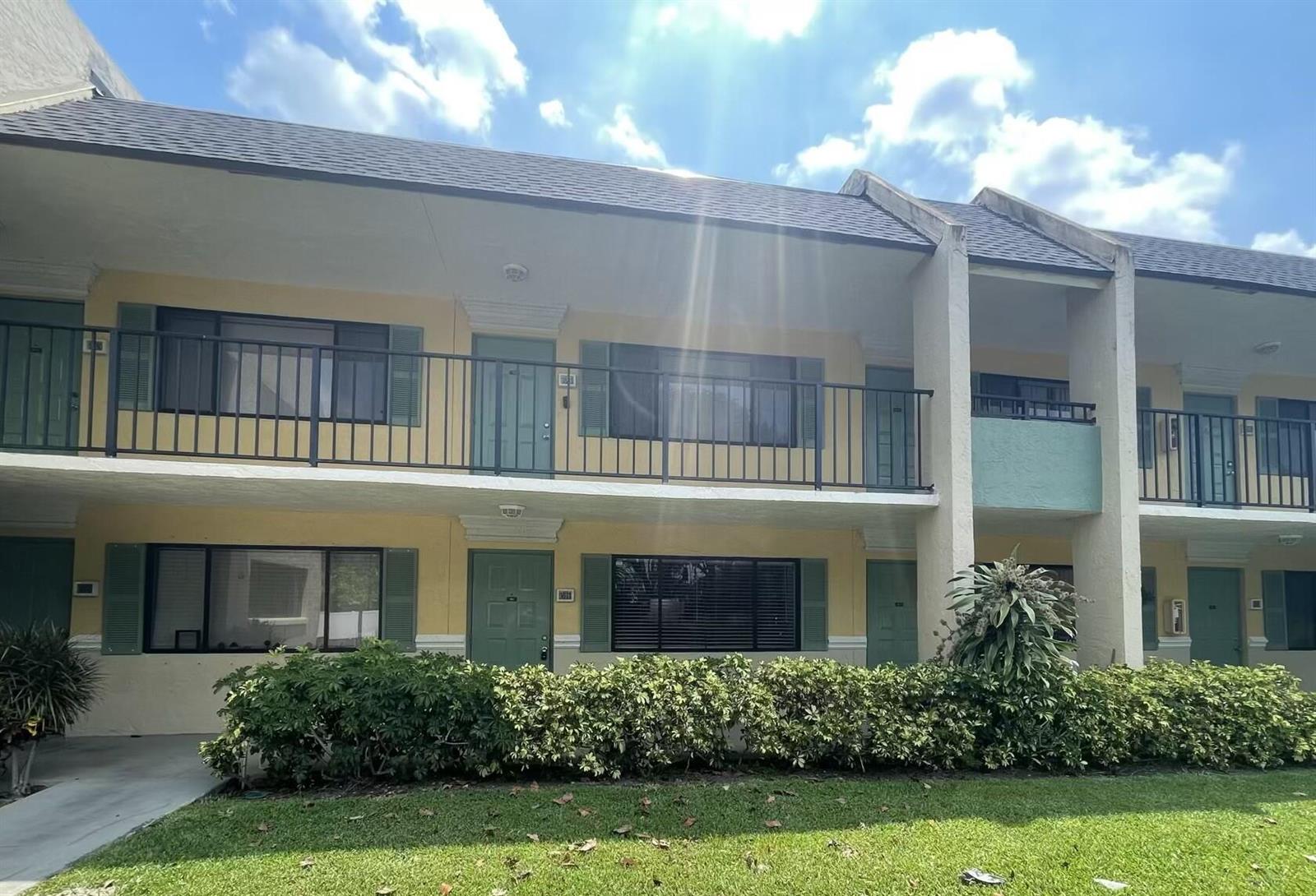 A two-story apartment building with yellow stucco walls, green doors, and a metal balcony railing — 1811 Meadows Circle W, Boynton Beach FL 33436, BOYNTON BEACH, FL