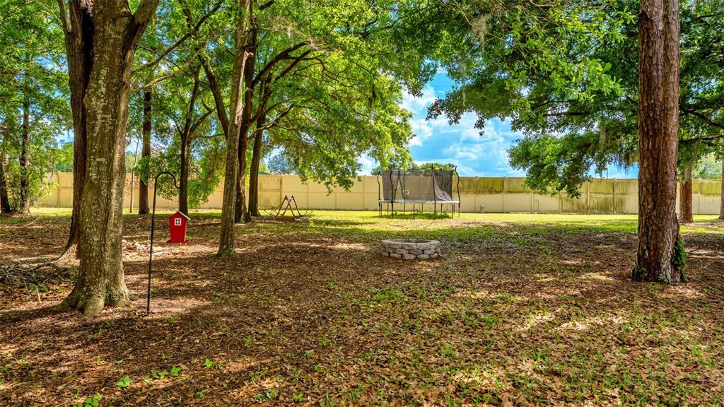 A backyard features large trees, a red birdhouse, a fire pit, and a trampoline — 1826 ALTAVISTA CIRCLE, LAKELAND, FL