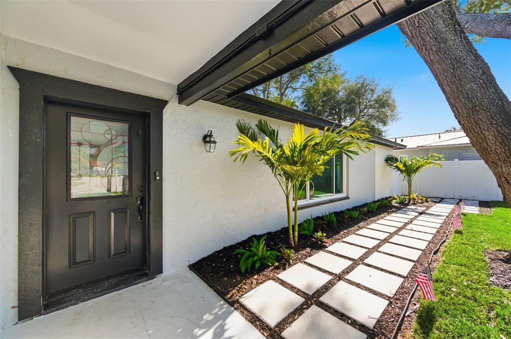 A white house exterior features a black front door, palm trees, and a stone walkway — 11180 113TH AVENUE, LARGO, FL