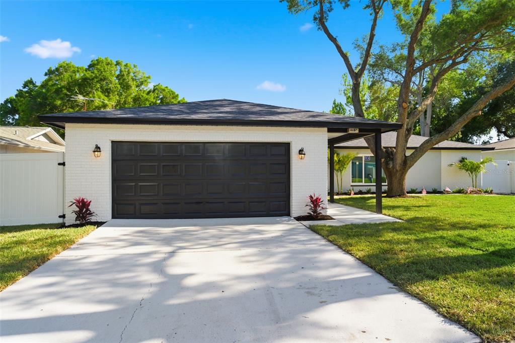 A white brick house features a dark garage door, a covered entryway, and a large tree — 11180 113TH AVENUE, LARGO, FL