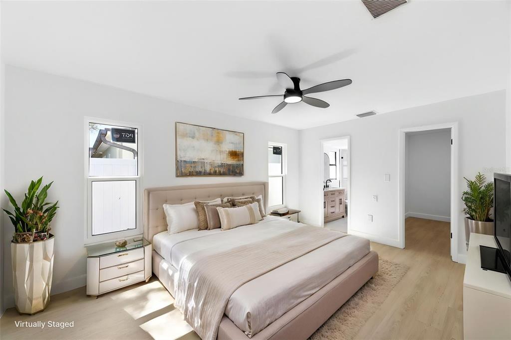 A bedroom features a tufted bed, light wood flooring, a ceiling fan, and two doorways — 11180 113TH AVENUE, LARGO, FL