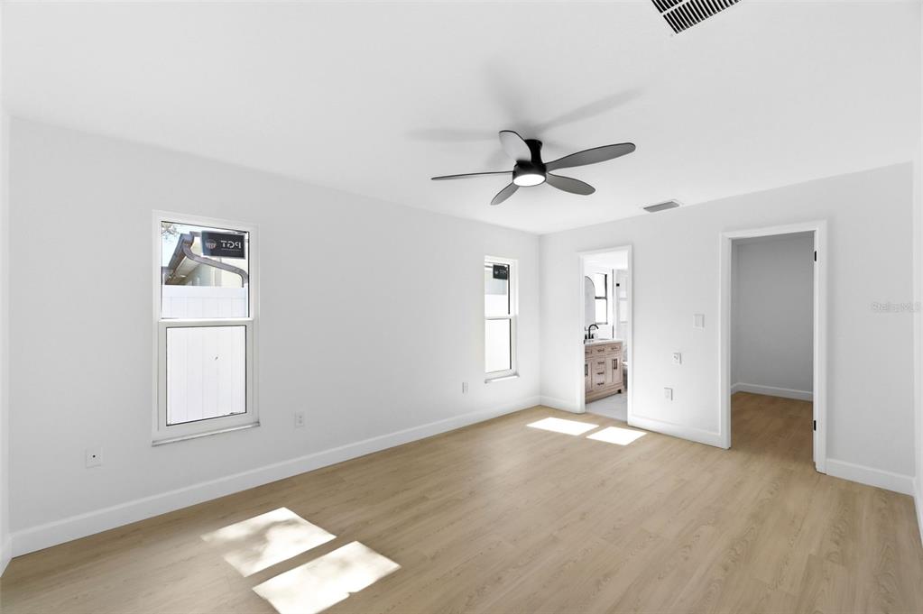 A bright bedroom features light wood-look flooring, white walls, a ceiling fan, and two windows — 11180 113TH AVENUE, LARGO, FL