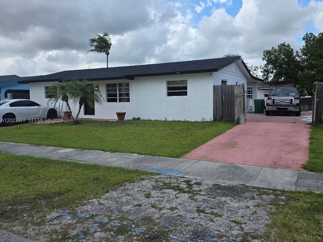 A single-story white house with a black roof, a red driveway, and a front lawn — HOMESTEAD, FL
