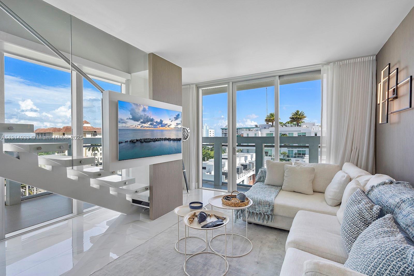 A modern living room features a floating staircase, a wall-mounted television, and floor-to-ceiling windows — 1150 101st St # 701, Bay Harbor Islands FL 33154, BAY HARBOR ISLANDS, FL