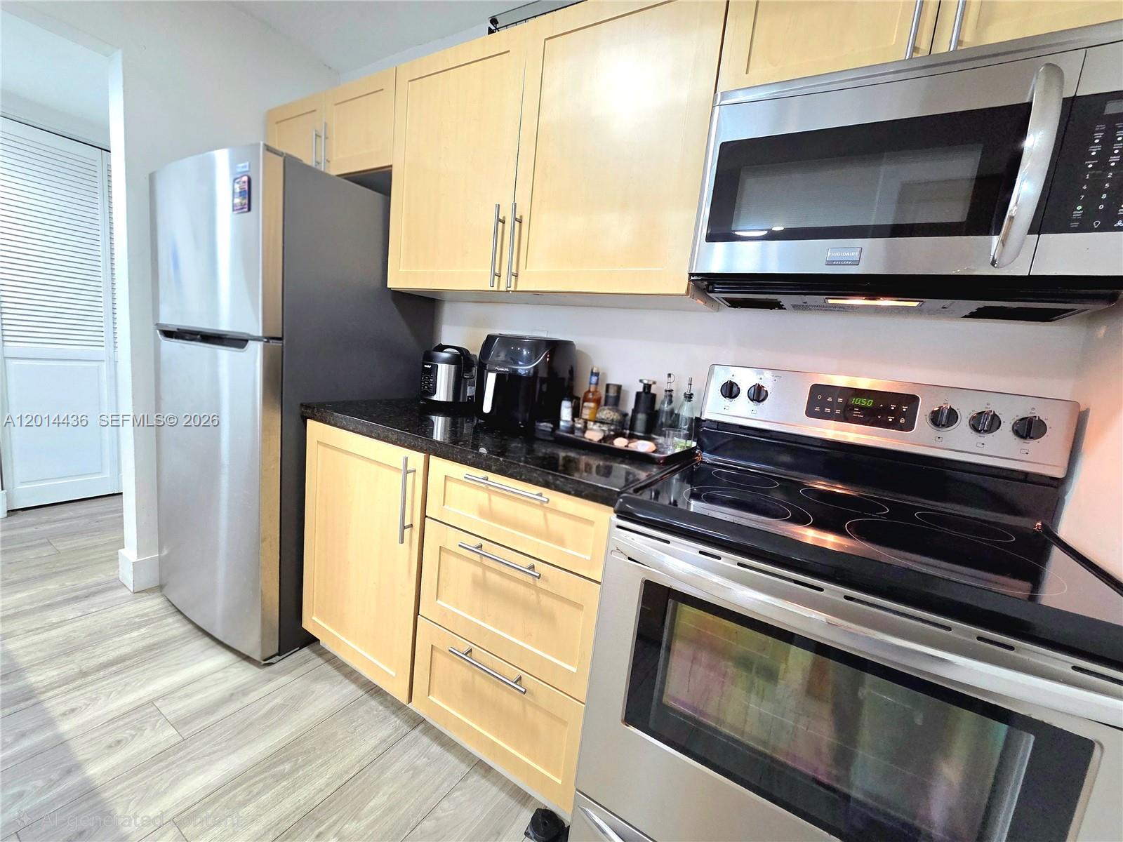 A kitchen features light wood cabinets, stainless steel appliances, and dark granite countertops — 7477 SW 82nd St # C115, Miami FL 33143, MIAMI, FL