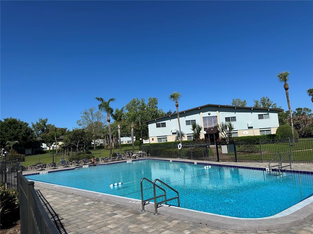 A swimming pool sits in front of a two-story apartment building with palm trees — 1695 LEE ROAD ROAD UNIT C110, WINTER PARK, FL