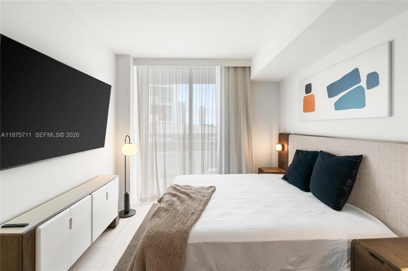 A modern bedroom features a bed, wall-mounted television, white cabinetry, and a balcony with curtains — 1611 SW 2nd Av # 504, Miami FL 33129, MIAMI, FL