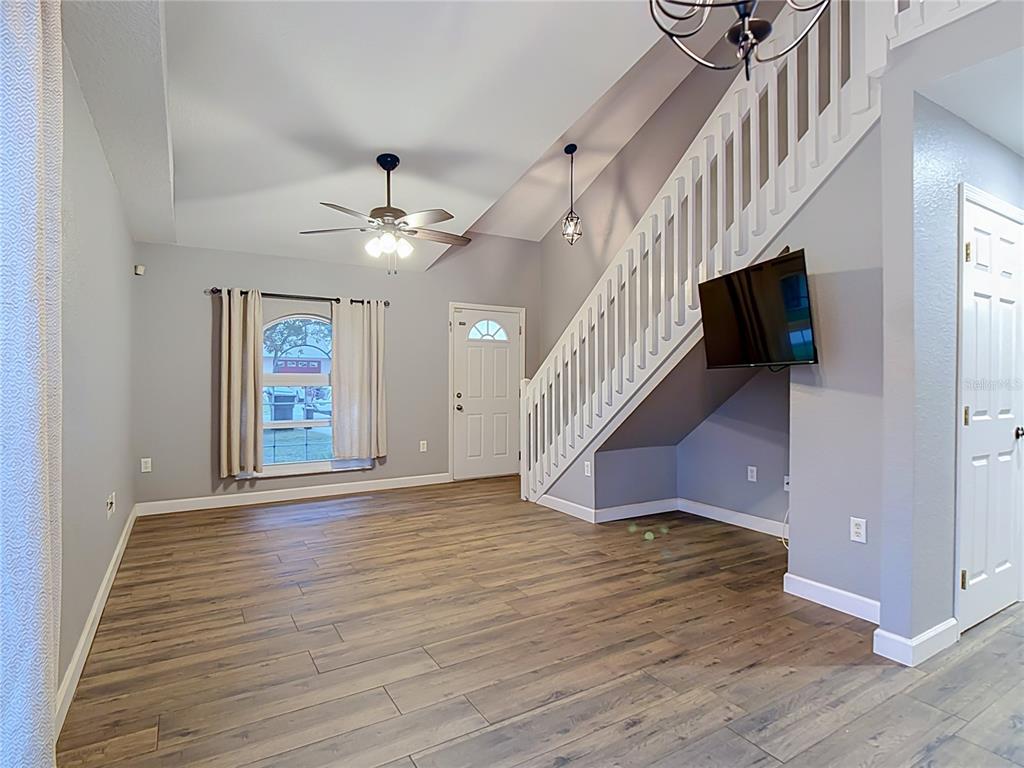 A living room features wood-look flooring, a staircase with white railings, and a wall-mounted television — 1436 SHIRLEY DRIVE, LAKELAND, FL