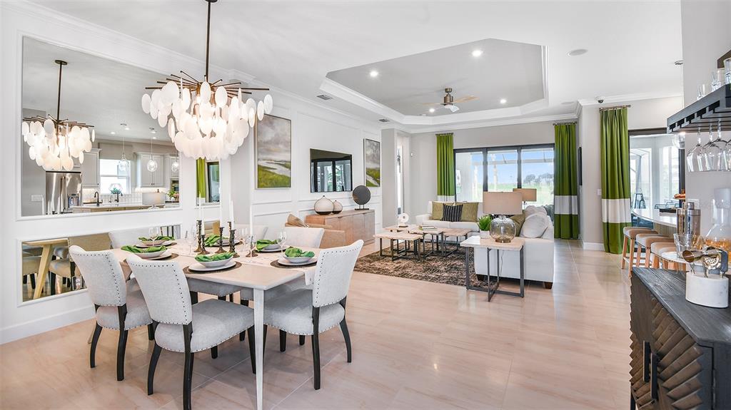 An open-concept dining and living area features a modern chandelier, light tile floors, and mirrors — 7712 MOONBEAM AVENUE, SARASOTA, FL