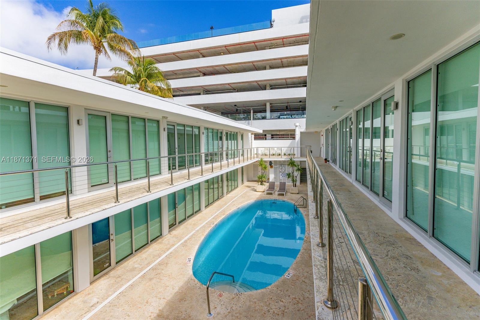 An outdoor swimming pool is situated between two levels of building units with glass doors — 1601 West Ave # 210, Miami Beach FL 33139, MIAMI BEACH, FL