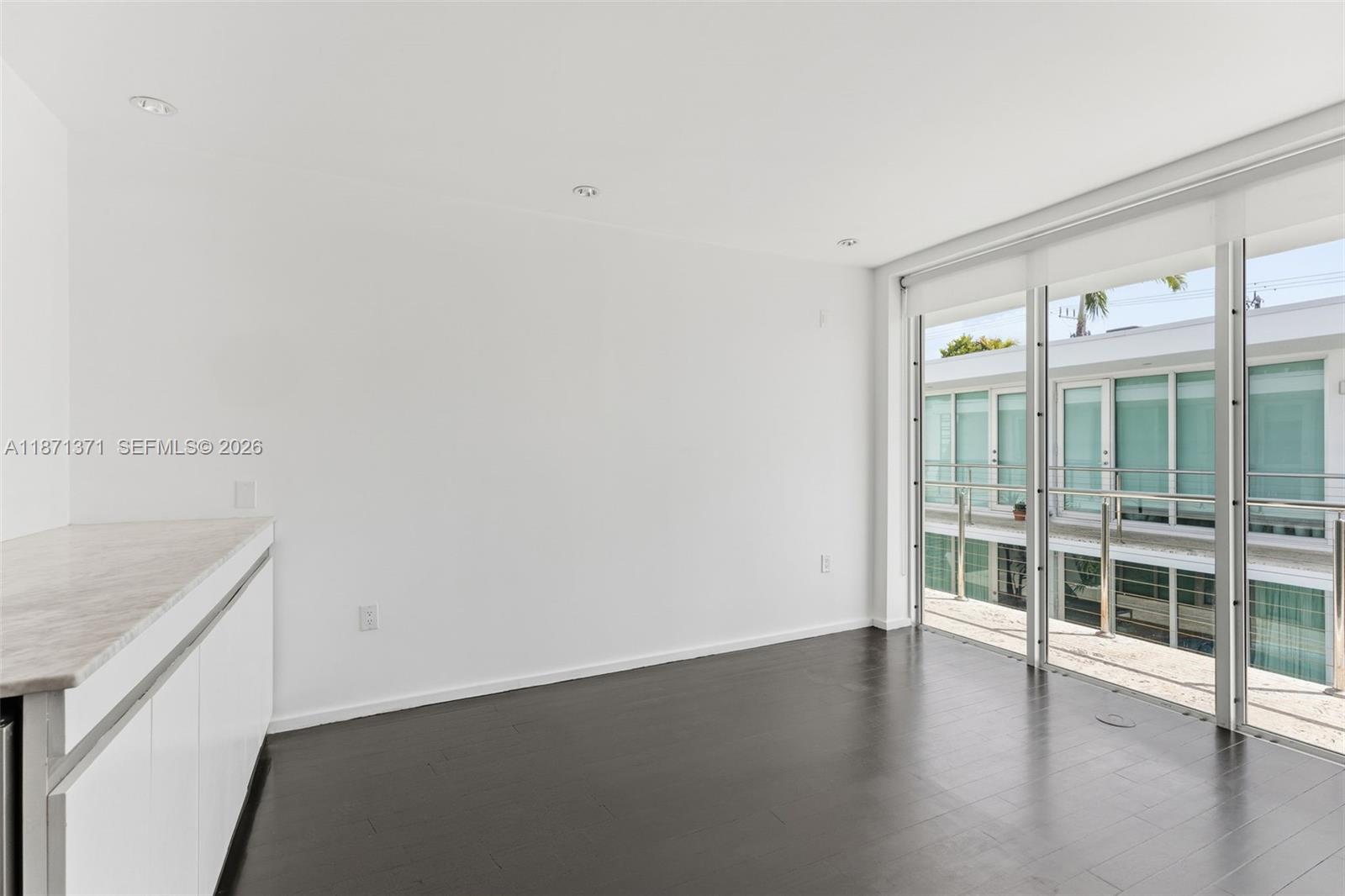 An empty room features dark wood flooring, white walls, and a sliding glass door to a balcony — 1601 West Ave # 210, Miami Beach FL 33139, MIAMI BEACH, FL