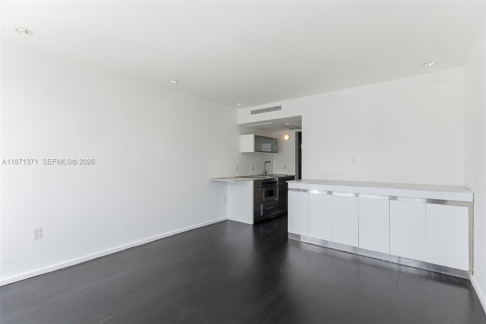 A minimalist kitchen features white cabinetry, dark wood flooring, and a stone-topped breakfast bar — 1601 West Ave # 210, Miami Beach FL 33139, MIAMI BEACH, FL