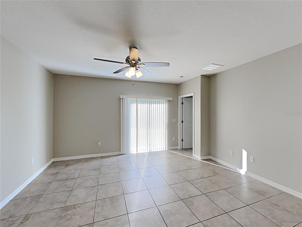 An empty room features light-colored walls, large floor tiles, a ceiling fan, and sliding glass doors — 15320 BROAD BRUSH DRIVE, RUSKIN, FL