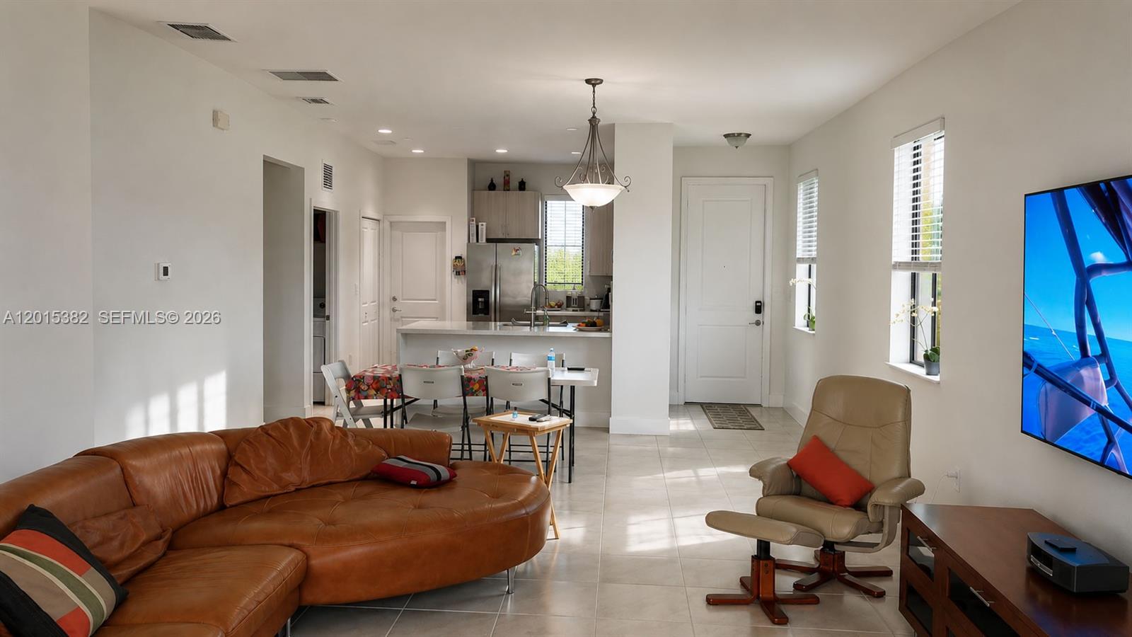 A living room with a brown leather sofa, tan recliner, and an open kitchen area — 4989 OFANTO LN, Ave Maria FL 34142, AVE MARIA, FL