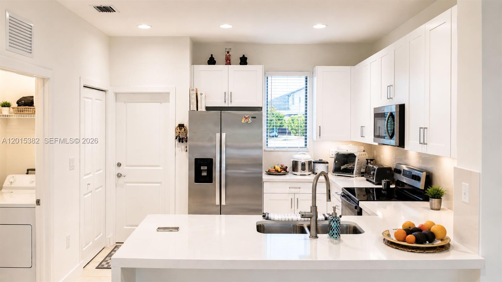 A modern kitchen features white cabinetry, stainless steel appliances, and a white quartz island countertop — 4989 OFANTO LN, Ave Maria FL 34142, AVE MARIA, FL