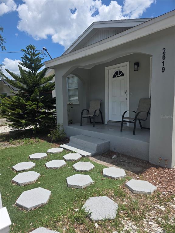 A gray house exterior features a covered porch with two chairs and hexagonal stepping stones — 2619 E CHELSEA STREET, TAMPA, FL