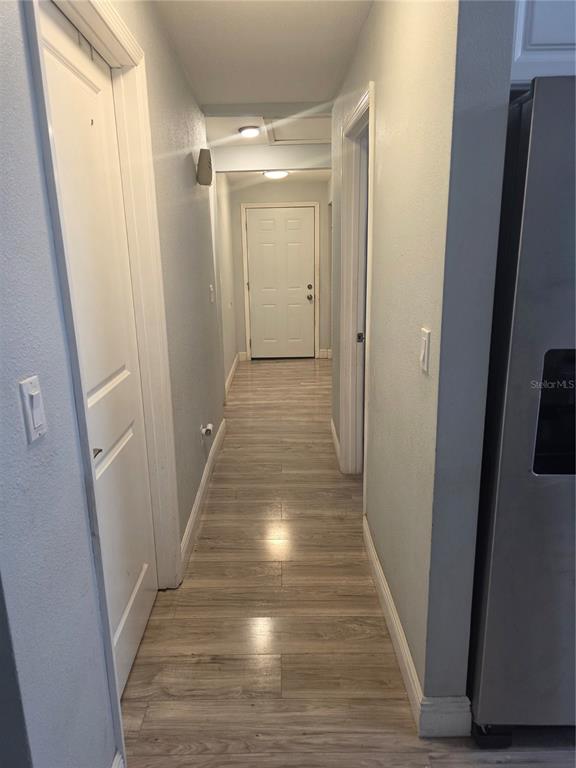 A hallway with light-colored wood-look flooring leads to a white door at the end — 2619 E CHELSEA STREET, TAMPA, FL