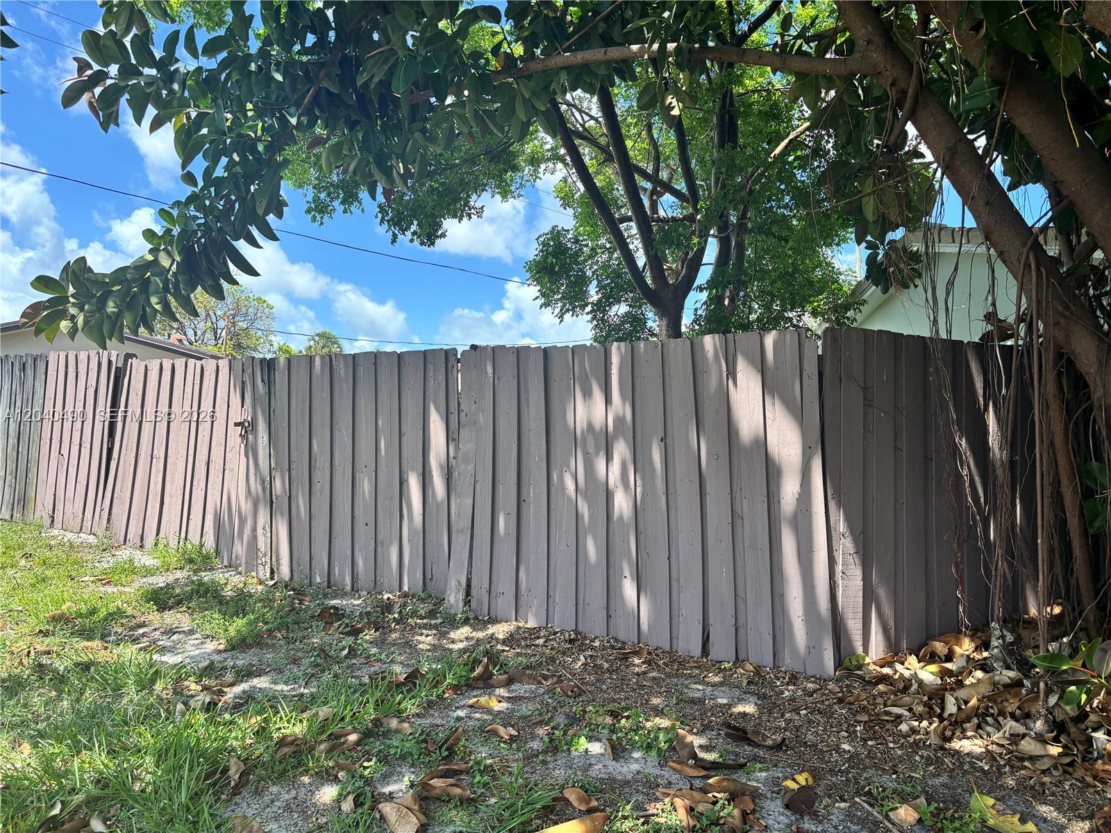 A weathered wooden fence stands in a yard beneath a large tree — 4300 NW 9th Ct, Coconut Creek FL 33066, COCONUT CREEK, FL