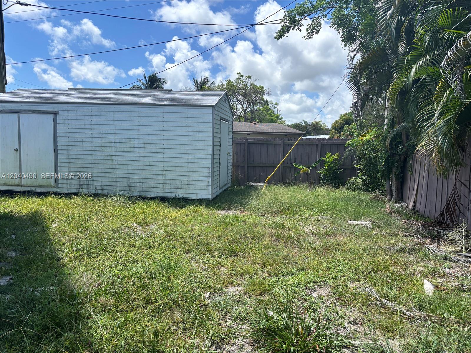 A white metal storage shed sits in a grassy backyard enclosed by a wooden fence — 4300 NW 9th Ct, Coconut Creek FL 33066, COCONUT CREEK, FL