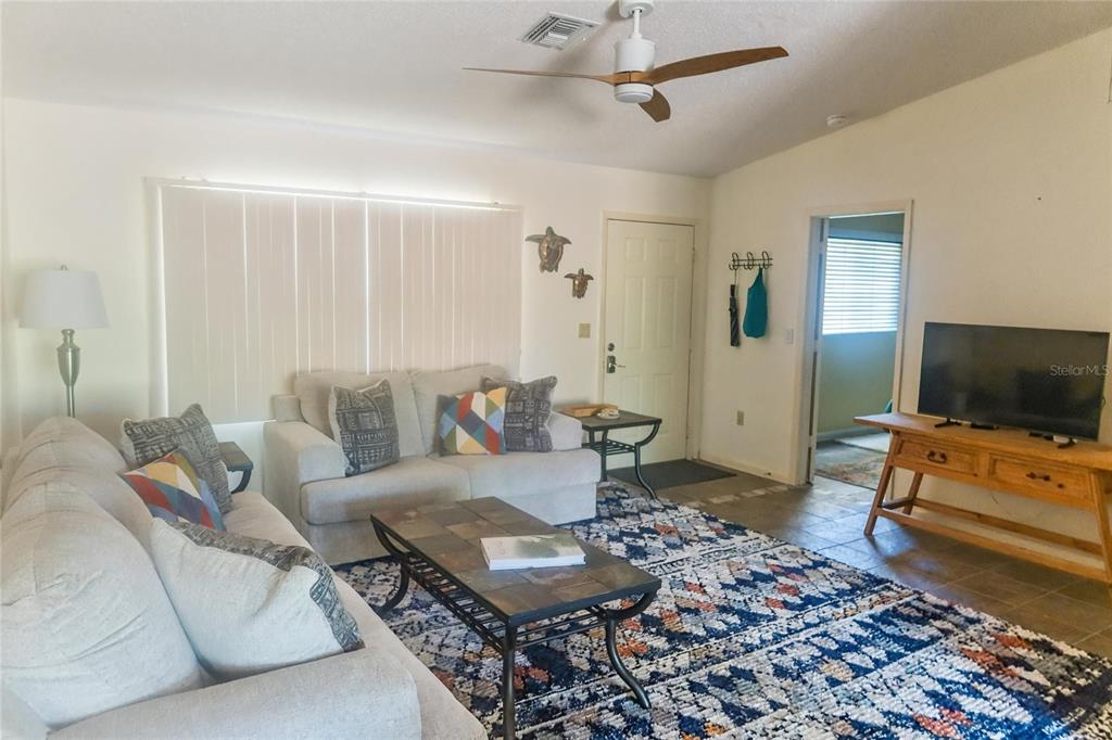 A living room features a light-colored sofa, a patterned area rug, and a television console — 9406 PROSPECT AVENUE, ENGLEWOOD, FL