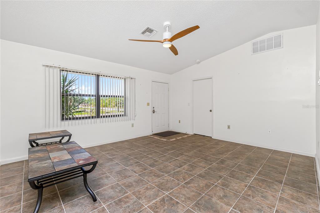 A living room with tiled floors, a ceiling fan, a window with blinds, and doors — 9406 PROSPECT AVENUE, ENGLEWOOD, FL