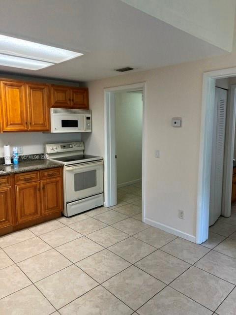 A kitchen features wood cabinets, a white stove, and light-colored tile flooring — TAMARAC, FL
