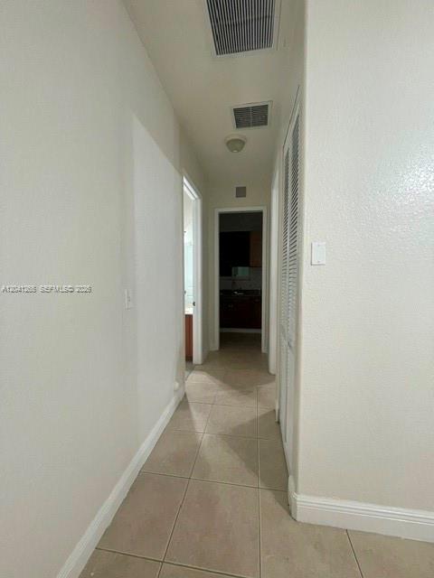 A hallway with light-colored tile flooring leads to a doorway showing a kitchen area — MIAMI, FL