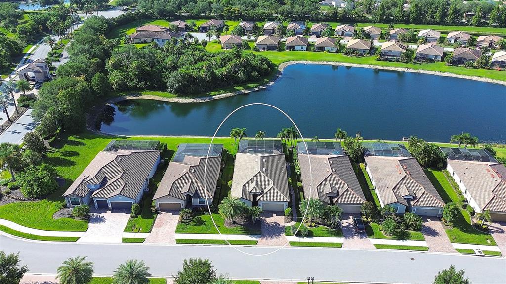 An aerial view shows a row of suburban houses with screened-in pools facing a lake — 7130 QUIET CREEK DRIVE, BRADENTON, FL