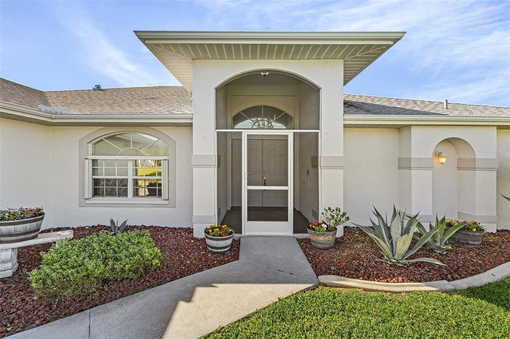 The exterior of a house features a covered entryway with a screen door and landscaping — 1230 SW 4TH AVENUE, CAPE CORAL, FL