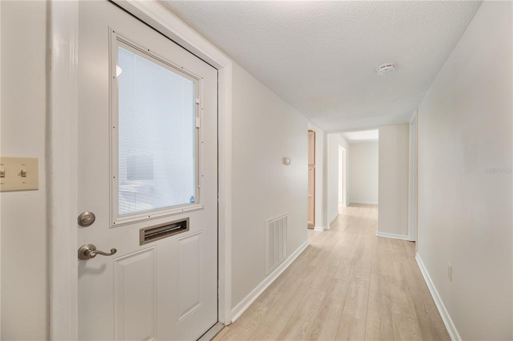A hallway with light wood-look flooring leads to an interior doorway and a white door — 616 COTTAGE LANE UNIT 616, LAKELAND, FL