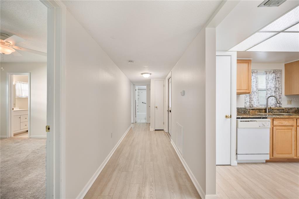 A hallway with light wood-look flooring connects to a kitchen on the right and a bathroom — 616 COTTAGE LANE UNIT 616, LAKELAND, FL