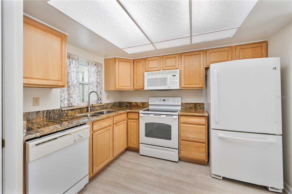 A kitchen features light wood cabinets, granite countertops, white appliances, and a drop ceiling — 616 COTTAGE LANE UNIT 616, LAKELAND, FL