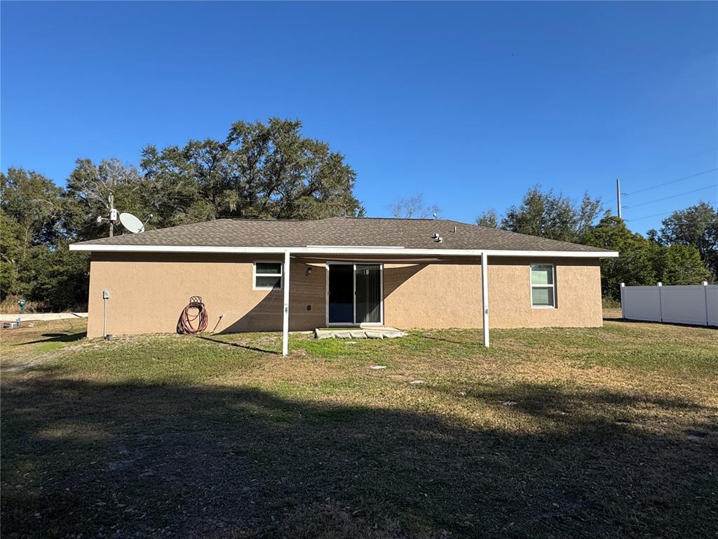 The exterior rear view of a tan stucco house features a sliding glass door and patio — 14476 SE 34TH COURT, SUMMERFIELD, FL