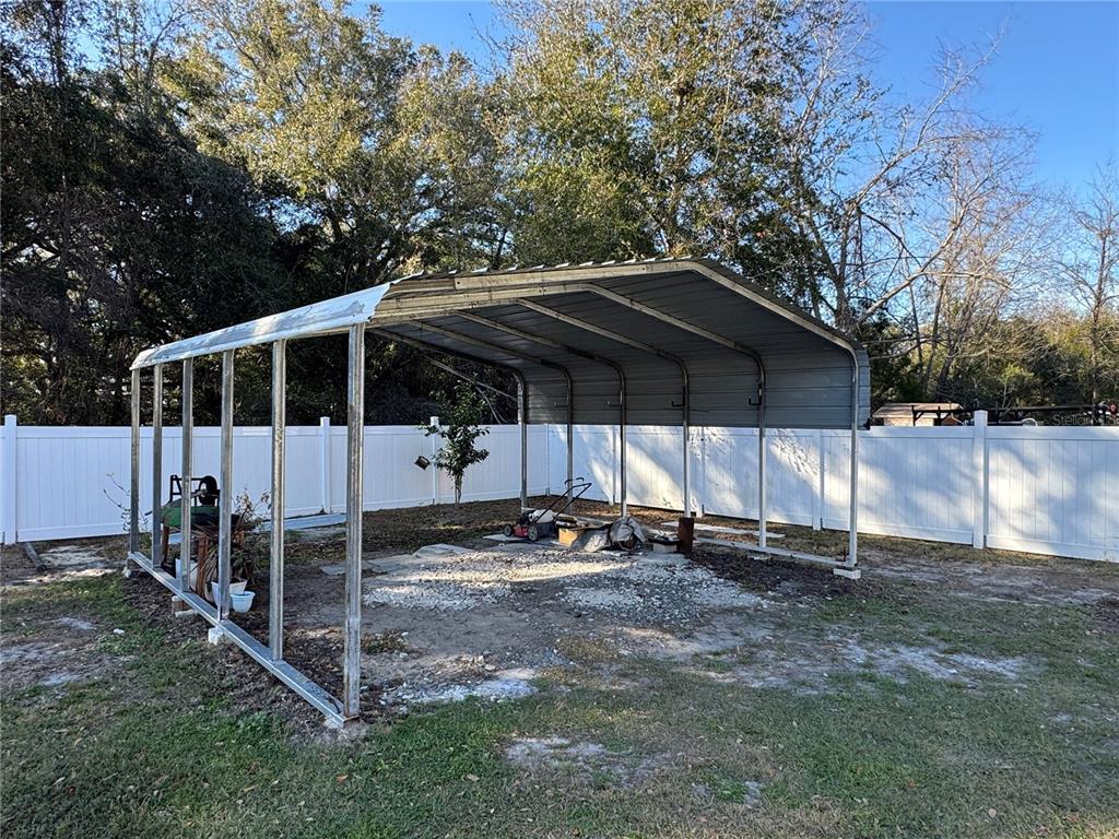 A metal carport stands in a backyard enclosed by a white vinyl privacy fence — 14476 SE 34TH COURT, SUMMERFIELD, FL