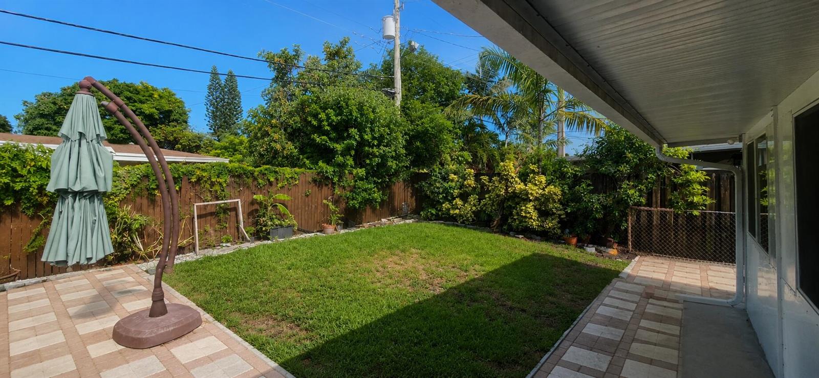 A backyard features a grassy lawn, a paved patio, a closed umbrella, and wooden fencing — 2311 N 58th Avenue, Hollywood FL 33021, HOLLYWOOD, FL