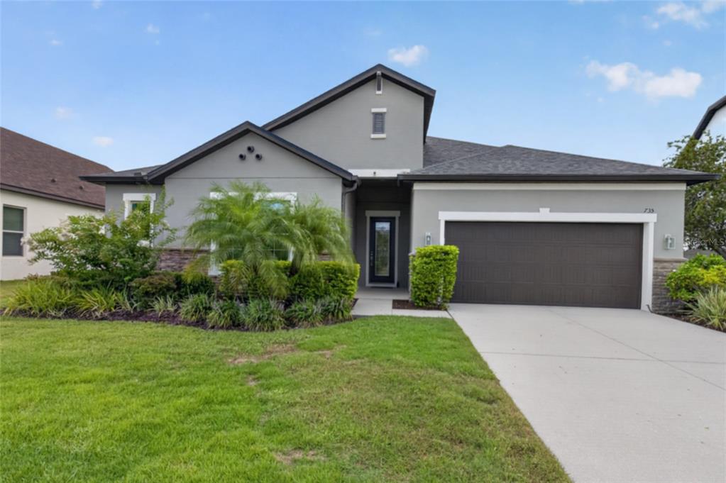 A gray single-story house features a two-car garage, a front entryway, and landscaped front yard — 735 116TH COURT NE, BRADENTON, FL