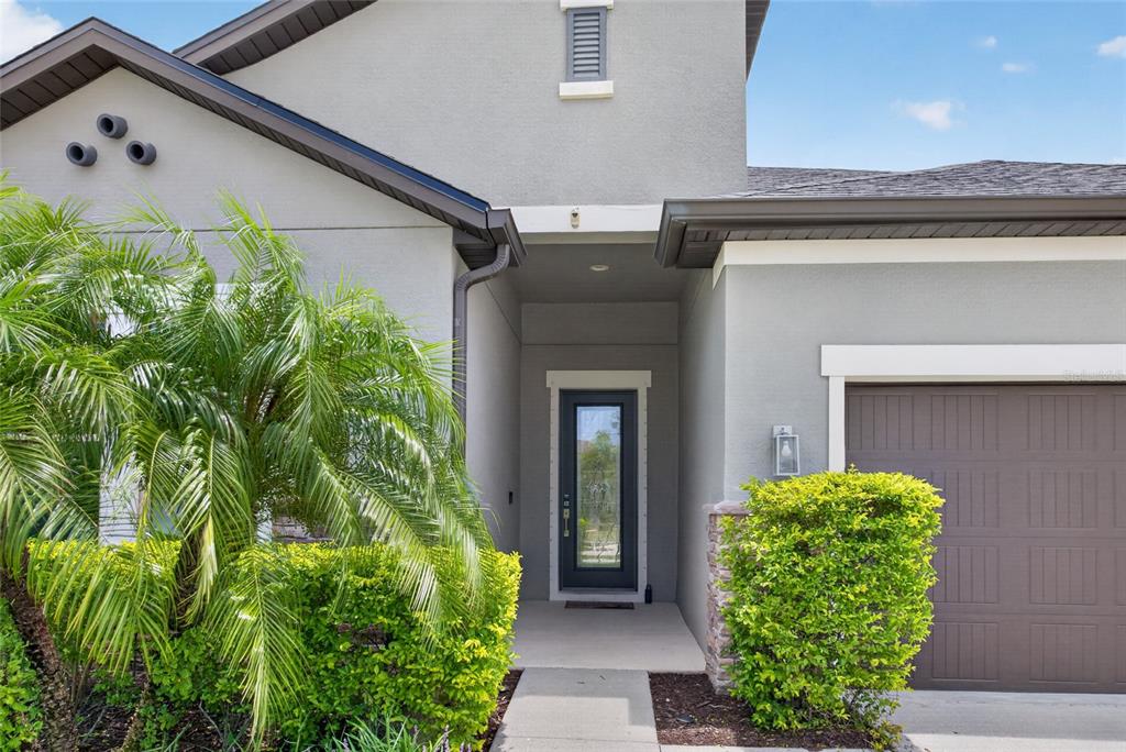 The exterior of a gray house features a front door, a garage, and landscaping — 735 116TH COURT NE, BRADENTON, FL