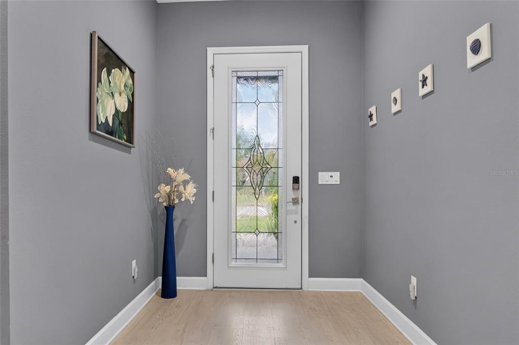 An entryway features gray walls, light wood-look flooring, a glass-paneled front door, and wall decor — 735 116TH COURT NE, BRADENTON, FL